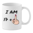White ceramic mug with the text “I Am 17+” and a cartoon female hand with pink nails showing a raised middle finger, rude 18th birthday mug.