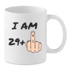 White mug with the text “I Am 29+” and a cartoon male hand showing a middle finger